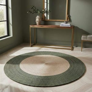 May include: A round area rug featuring a natural tan center and a wide, dark olive green border. The rug is constructed with a braided texture, creating a circular pattern that radiates from the middle toward the outer edge of the floor covering.