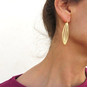 Può includere: Orecchini dorati con un design geometrico a forma di foglia. Gli orecchini sono pendenti e hanno uno stile semplice e moderno.