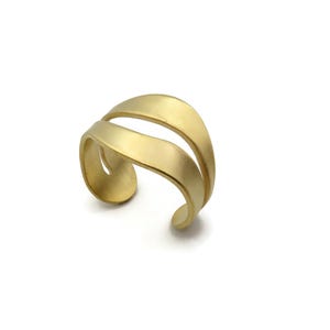 Könnte beinhalten: Ein goldfarbener Ring mit einem Doppelband-Design und einer glatten, matten Oberfläche. Der Ring hat eine offene Struktur mit zwei geschwungenen, parallelen Bändern, die sich um den Finger legen und ein geschichtetes Aussehen erzeugen.