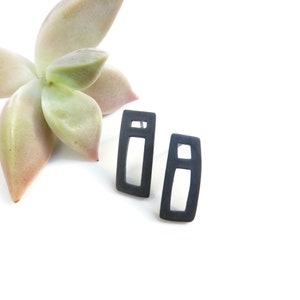 May include: A pair of black geometric earrings with a rectangular shape and a smaller rectangle cut out in the centre.