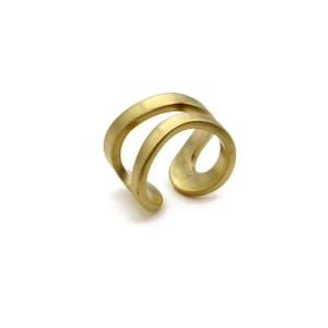 May include: A gold-toned metal ring featuring a double-band design with a smooth, matte finish. The ring has an open, bypass-style structure where the two bands curve and connect at one side, creating a continuous, fluid, and rounded silhouette.