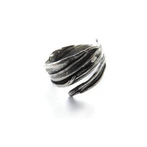 May include: A silver ring with a textured, organic design that resembles a leaf or branch. The ring is open and adjustable.