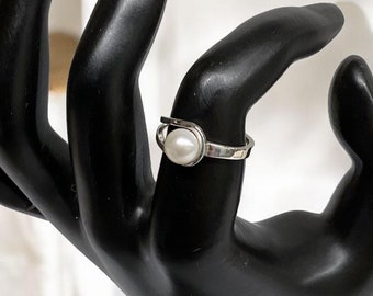 May include: A silver ring with a white pearl set in a curved band.