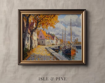 May include: Framed landscape painting of a European coastal town with boats docked in the harbor. The artwork features buildings with red-tiled roofs, a cobblestone path, and trees with golden leaves. The frame is dark brown with a gold inner edge. Text: Isle & Pine Art Collection.