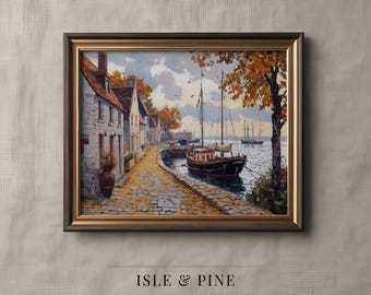 May include: Framed art print of a coastal scene with a cobblestone path, buildings, and a sailboat. The artwork features warm autumn colors, with a brown frame and the text "ISLE & PINE ART COLLECTION" at the bottom.