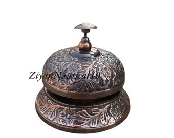 Puede incluir: Una campana de bronce con intrincados diseños florales. La campana tiene una parte superior redondeada y una base acampanada, con un pequeño mango. El texto "Ziyan Nautical10" es visible en el lateral.