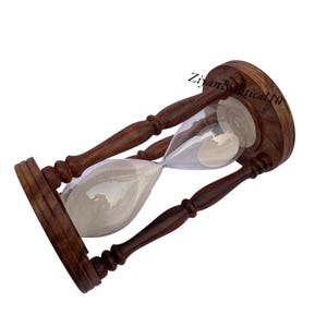 May include: A wooden hourglass with a clear glass center filled with light-colored sand. The hourglass has a dark brown wooden frame and handles. The text "Ziyan Nautical10" is visible on the top of the hourglass.