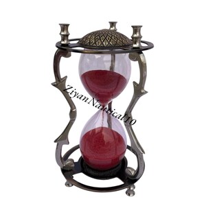 May include: An hourglass with a decorative metal frame and a patterned top. The glass bulbs contain red sand. The text "Ziyan Nautical 10" is printed on the glass. The hourglass is a vintage-style decorative item.