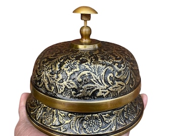 May include: An antique-style brass bell with intricate floral patterns. The bell has a dark background with gold accents and a small handle on top. The base of the bell also features floral designs. The text "ZiyanNautical10" is visible on the base.