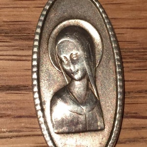 May include: Silver oval pendant with a raised image of a woman wearing a veil. The pendant has a beaded border and a small letter 'R' at the bottom.