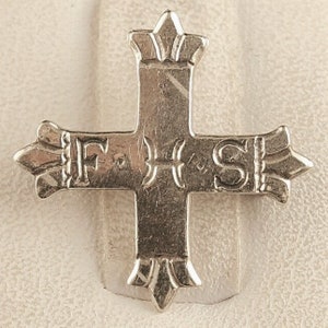 Può includere: Un ciondolo a forma di croce color argento con decorazioni ornate a forma di corona alle estremità di ogni braccio. La croce presenta le lettere "FHS" incise sulla barra orizzontale, con un design stilizzato. Il ciondolo è probabilmente in metallo.