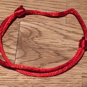 Puede incluir: Un brazalete de cuerda roja con dos nudos en los extremos.