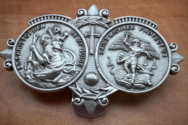 May include: Silver-toned metal religious pendant featuring three circular medallions with images of Saint Christopher, Saint Michael, and a cross. The Saint Christopher medallion has the text "St. Christopher Be My Guide". The Saint Michael medallion has the text "Saint Michael Protect Us".