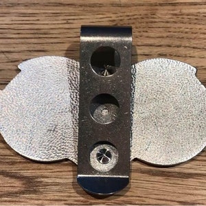 May include: Silver-toned metal belt buckle with a decorative design. The buckle has a clip on the back for attaching to a belt.