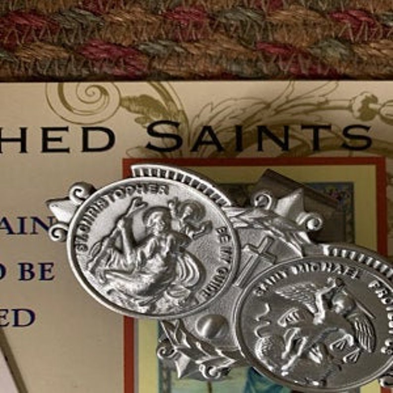 May include: Silver metal religious charm with three round medallions featuring images of saints. The medallions are surrounded by a decorative border with a cross and a star.