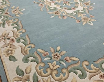 Può includere: Un tappeto rettangolare azzurro con un design floreale ornato. Il tappeto presenta un medaglione centrale e un bordo con motivi floreali color crema, verdi e beige. Il design del tappeto include foglie e motivi floreali.