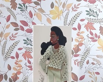 May include: A greeting card featuring an illustration of a person with dark skin and long black hair, wearing a textured light green knit sweater over a gold top and light green trousers, with the handwritten name Willie Hillard on the side.