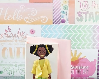 May include: A greeting card featuring a paper doll illustration of a person with dark skin and black hair in pigtails, wearing a yellow cardigan over a yellow top and green patterned pants, set against a light pink cardstock background.