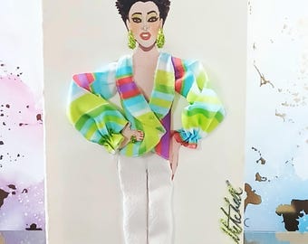 May include: A mixed-media art piece featuring a stylized figure with short dark hair, wearing lime green earrings, a multi-colored striped wrap top with voluminous sleeves, and white trousers. The name 'Willie Mitchell' is written in gold script.