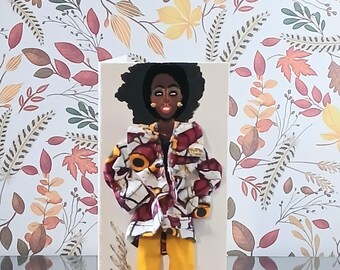 May include: A greeting card featuring a three-dimensional illustration of a person with dark skin and black hair, wearing a patterned maroon, white, and yellow jacket over solid yellow trousers. The card includes gold cursive text on the left side.