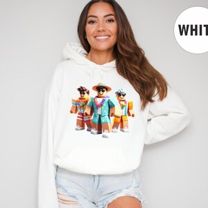 Puede incluir: Sudadera con capucha blanca con un gr&aacute;fico de tres personajes de Roblox con atuendos de vacaciones. Los personajes llevan gafas de sol, sombreros y camisas hawaianas. La sudadera tiene una capucha con cord&oacute;n y un bolsillo delantero. La palabra "WHITE" est&aacute; en un c&iacute;rculo blanco.