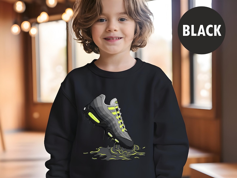 May include: Black sweatshirt featuring a graphic of a gray and black sneaker with neon green accents. The sneaker is depicted with a splash effect. A black circle with the word "BLACK" is in the upper right corner.
