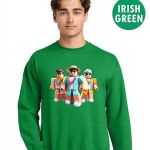 Puede incluir: Una sudadera verde con un gr&aacute;fico de tres personajes de dibujos animados con ropa de playa. Los personajes llevan gafas de sol, sombreros y guirnaldas de flores. La sudadera tiene las palabras "Irish Green" en un c&iacute;rculo verde.