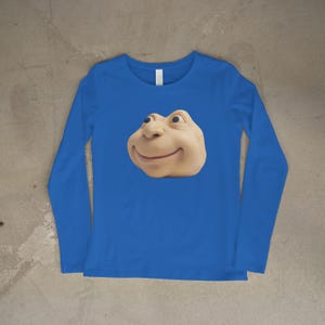 May include: A long-sleeved, royal blue top with a smiling, light-brown cartoon face. The face has a large nose, small eyes, and a wide, curved mouth. The top has a crew neck and is made of a soft material.