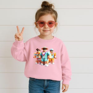 Puede incluir: Una sudadera rosa claro con un gr&aacute;fico de tres personajes de Roblox con ropa de vacaciones. Los personajes llevan gafas de sol, sombreros y camisas hawaianas. La sudadera la lleva un ni&ntilde;o peque&ntilde;o con gafas de sol en forma de coraz&oacute;n.
