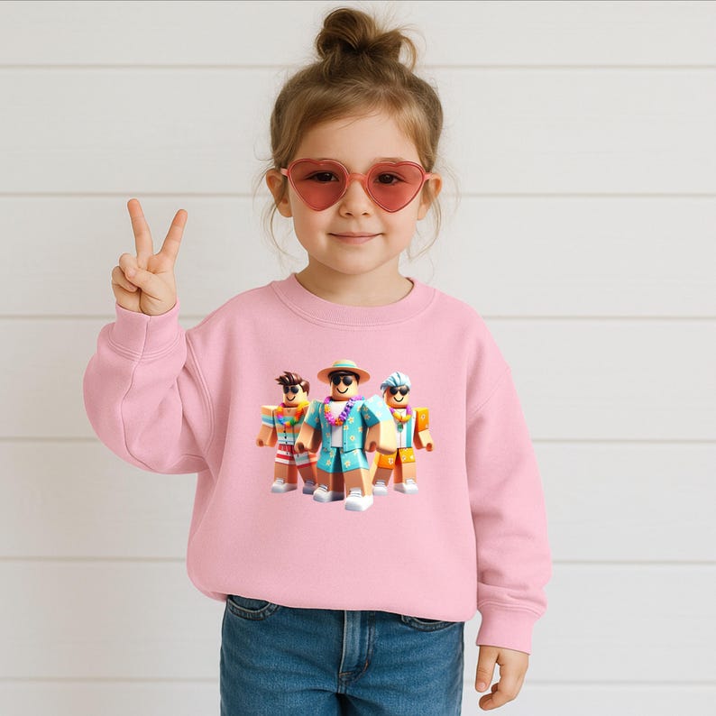 Puede incluir: Una sudadera rosa claro con un gr&aacute;fico de tres personajes de Roblox con ropa de vacaciones. Los personajes llevan gafas de sol, sombreros y camisas hawaianas. La sudadera la lleva un ni&ntilde;o peque&ntilde;o con gafas de sol en forma de coraz&oacute;n.