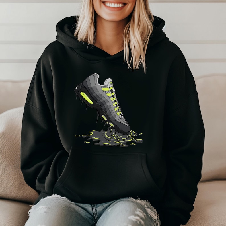 May include: Black hoodie featuring a graphic of a gray and black sneaker with neon green accents. The sneaker is depicted in a puddle of dark green liquid. The hoodie has a front pocket and a hood.