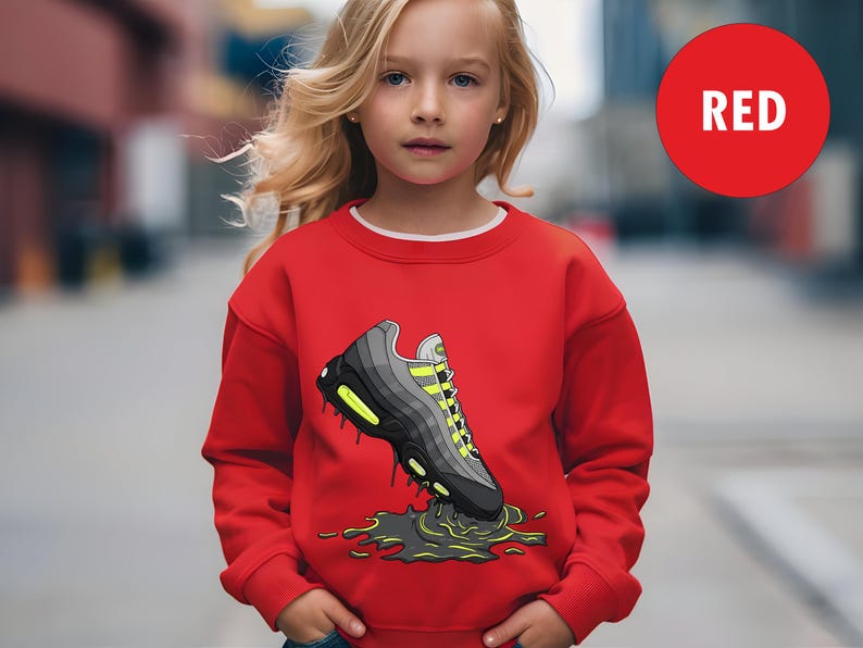 May include: A red sweatshirt featuring a graphic of a sneaker with black, gray, and neon yellow accents. The word "RED" is in a red circle in the upper right corner. The sweatshirt is worn by a young person.