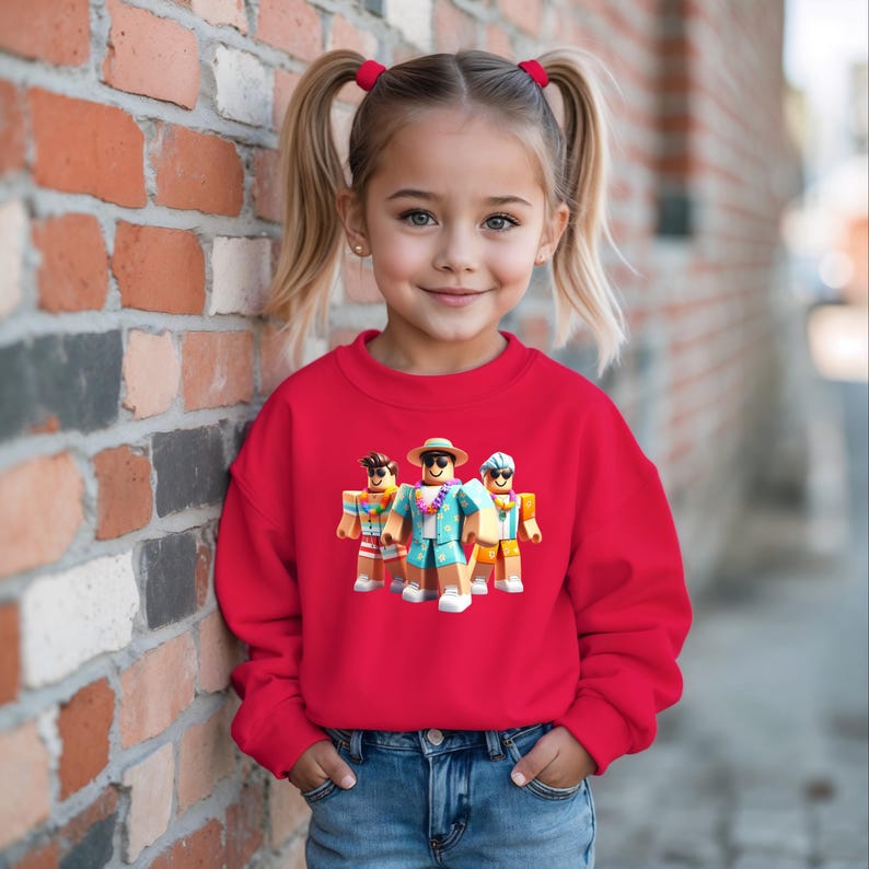 Puede incluir: Una ni&ntilde;a peque&ntilde;a con una sudadera roja brillante con un gr&aacute;fico de tres personajes de dibujos animados con ropa de playa. Los personajes llevan gafas de sol, sombreros y camisas hawaianas. La ni&ntilde;a tambi&eacute;n lleva vaqueros azules.
