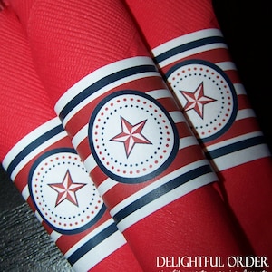 May include: Red and white striped napkin rings with a blue star design. The napkin rings are decorated with a white circle with a blue star and red dots.