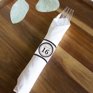 Könnte beinhalten: Weiße Serviette mit einem schwarz-weißen Serviettenring, auf dem "Sweet 16" steht. Die Serviette ist um eine durchsichtige Plastikgabel gewickelt.