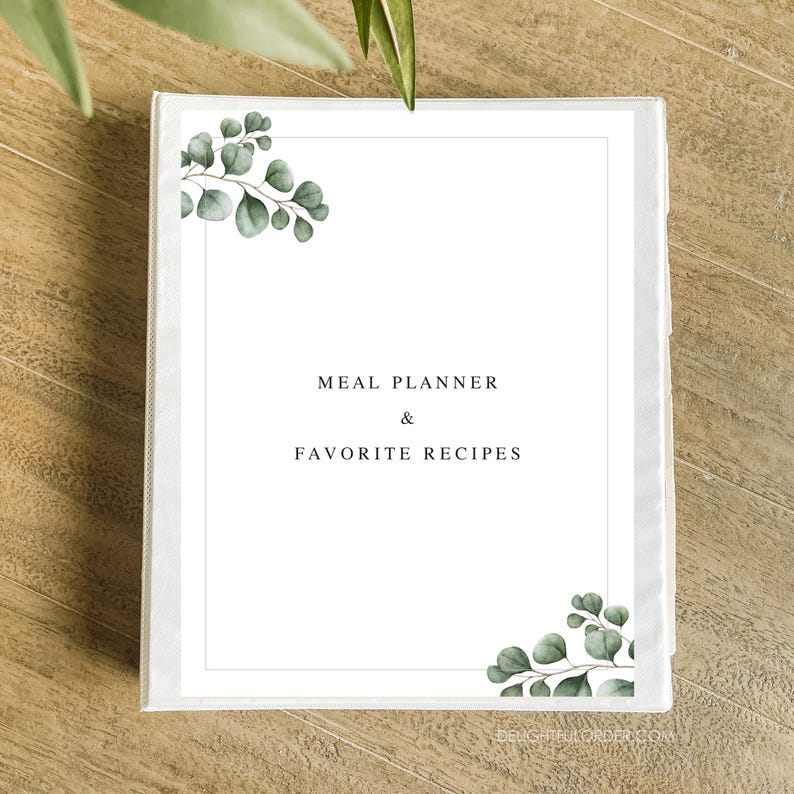 Puede incluir: Carpeta blanca con un dise&ntilde;o de hojas verdes en la portada. El texto "MEAL PLANNER & FAVORITE RECIPES" est&aacute; impreso en negro en la parte delantera.