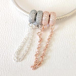 Può includere: Primo piano di tre braccialetti con ciondoli con catenine pendenti. Due ciondoli sono argentati con pietre trasparenti e uno è in oro rosa con pietre trasparenti. I braccialetti sono su una catena d'argento.