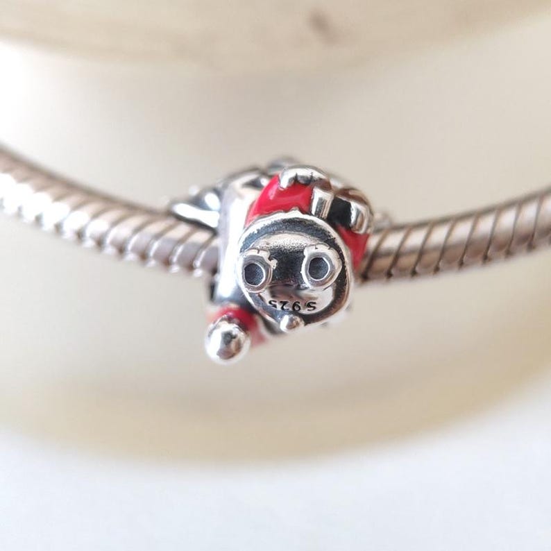 May include: A silver charm in the shape of a red and silver train engine. The charm has two round black eyes and the text "S925" is visible. The charm is attached to a silver bracelet.
