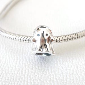 Op de afbeelding: Een zilveren bedel in de vorm van een vriendelijke geest. De geest heeft kleine, donkere ogen en een lichtjes geopende mond. De bedel is bevestigd aan een zilveren armband.
