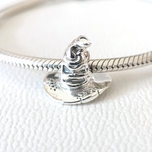 Op de afbeelding: Een zilveren bedel in de vorm van een tovenaars hoed. De hoed is gedetailleerd met getextureerde lijnen en een brede rand. De bedel is bevestigd aan een zilveren armband, wat het ontwerp en vakmanschap laat zien.