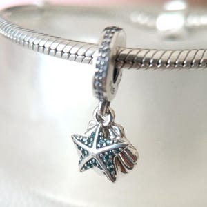 May include: A silver charm with a starfish and seashell design. The starfish has turquoise accents and is suspended from a beaded ring. The charm is attached to a silver snake chain bracelet. The jewelry is suitable for ocean-themed accessories.