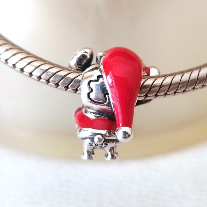 May include: A silver charm featuring a Santa Claus design with a red hat and coat. The charm is attached to a silver bracelet. The Santa Claus charm has a detailed design and is marked with "S925".