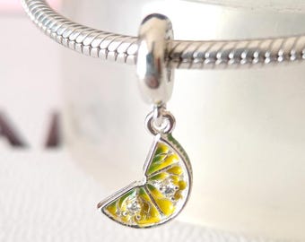 May include: A silver charm with a lemon slice design. The charm features a yellow and green enamel lemon slice with two clear crystals. The charm is attached to a silver bracelet.