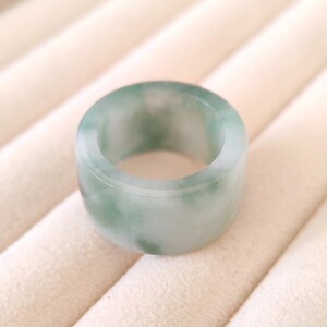K&ouml;nnte beinhalten: Ein breiter, runder Ring aus Jade. Der Ring hat eine hellgr&uuml;ne Farbe mit wei&szlig;en Marmorierungen. Der Ring ist glatt und poliert. Der Ring scheint ein massives St&uuml;ck Jade zu sein.