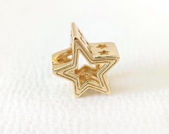 May include: A gold-colored star-shaped charm with a layered design. The charm features a hollow center and small star cutouts on the top surface. The star is a bright, shiny gold color.