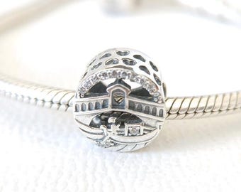 May include: A silver charm with a detailed bridge design, accented with small clear stones. The charm is cylindrical with a perforated top and is displayed on a silver chain.