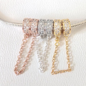 May include: Close-up of five decorative charm beads in rose gold, silver, and gold tones. Each bead is encrusted with small, clear crystals and connected to a chain. The beads are displayed on a silver bracelet.