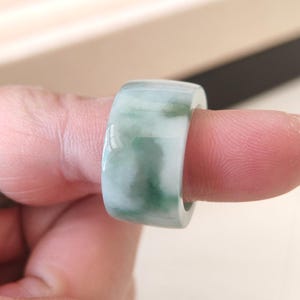 K&ouml;nnte beinhalten: Ein Jade-Ring mit glatter, polierter Oberfl&auml;che. Der Ring weist eine Mischung aus wei&szlig;en und gr&uuml;nen Farbt&ouml;nen auf, die einen Marmoreffekt erzeugt. Der Ring ist im breiten Bandstil gehalten.