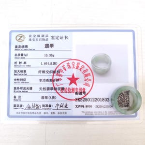 K&ouml;nnte beinhalten: Ein Jade-Ring und eine Jade-Scheibe liegen auf einem Zertifikat. Das Zertifikat enth&auml;lt chinesischen Text und Details zu den Eigenschaften des Jades, einschlie&szlig;lich Gewicht (10,35 g) und Brechungsindex (1,66). Ein roter Stempel mit chinesischem Text ist ebenfalls sichtbar.