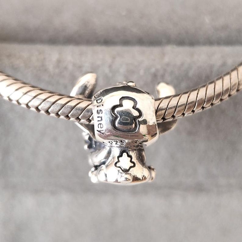 Puede incluir: Un charm de plata con un dise&ntilde;o de Disney, que presenta un personaje con orejas grandes y un cuerpo peque&ntilde;o. El charm est&aacute; unido a una pulsera de plata. El charm tiene la inscripci&oacute;n "Disney" y "925".